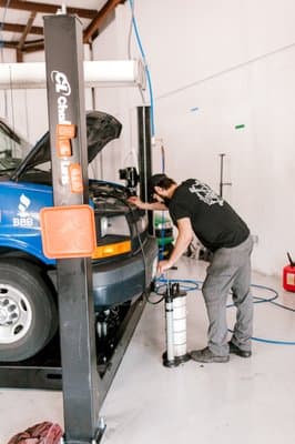 A technician is inspecting or repairing a vehicle on a hydraulic lift at Knight’s Mobile Auto Maintenance & Repair in Chesapeake, VA.